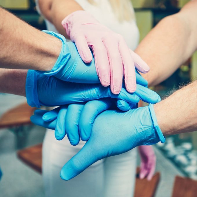 Teamwork of the doctors in hospital. Hands of four men in blue gloves and one woman in pink gloves. Themes health care, cooperation, trust and success.